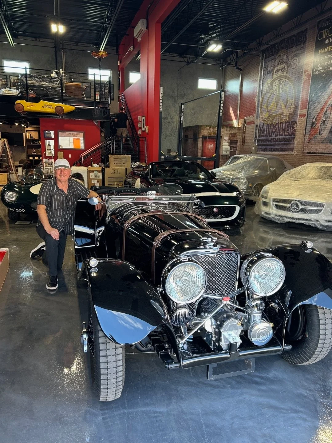 Lex standing beside his newly delivered SS100 in his garage, surrounded by other classic sports cars.